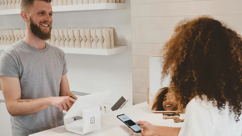 A cheerful customer is completing a payment at a modern checkout counter, smiling as they interact with the cashier. The sleek, contemporary design of the checkout area enhances the customer experience, reflecting efficiency and satisfaction in a professional environment